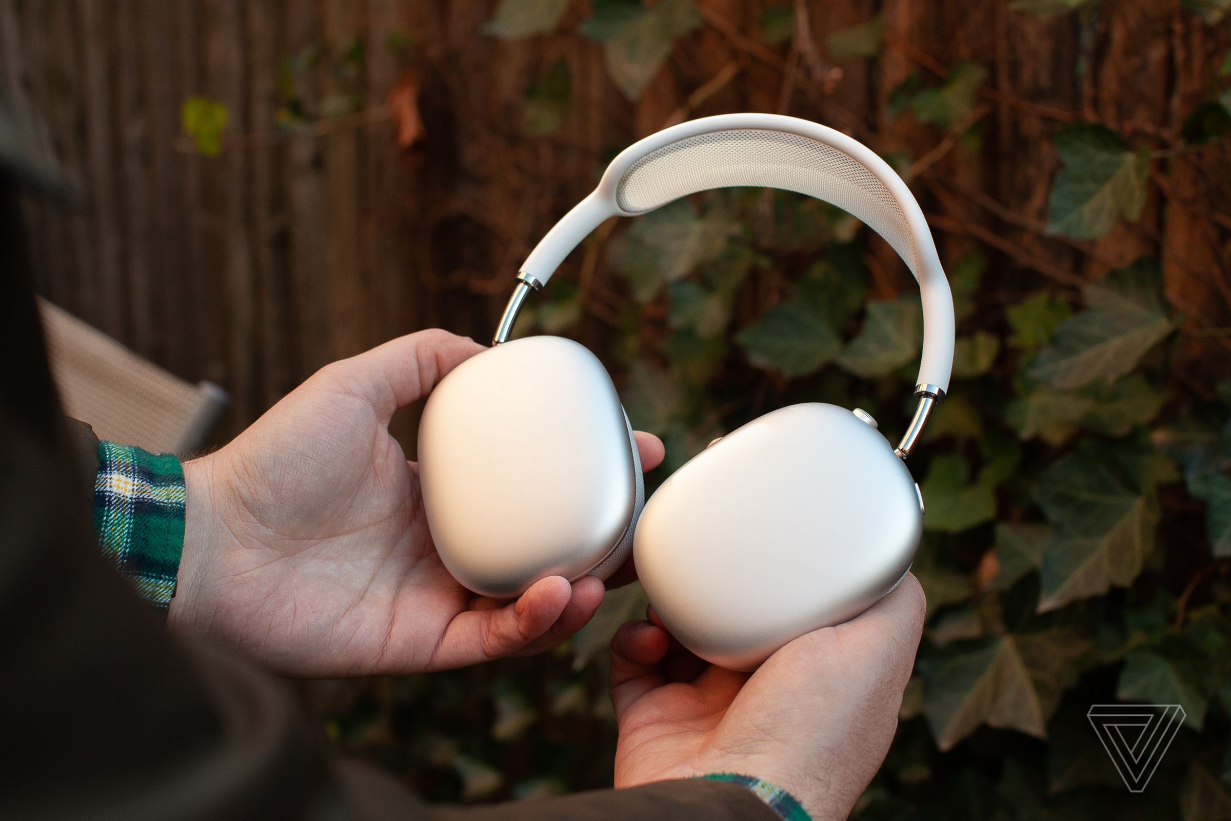 A hand holding the silver Apple AirPods Max.