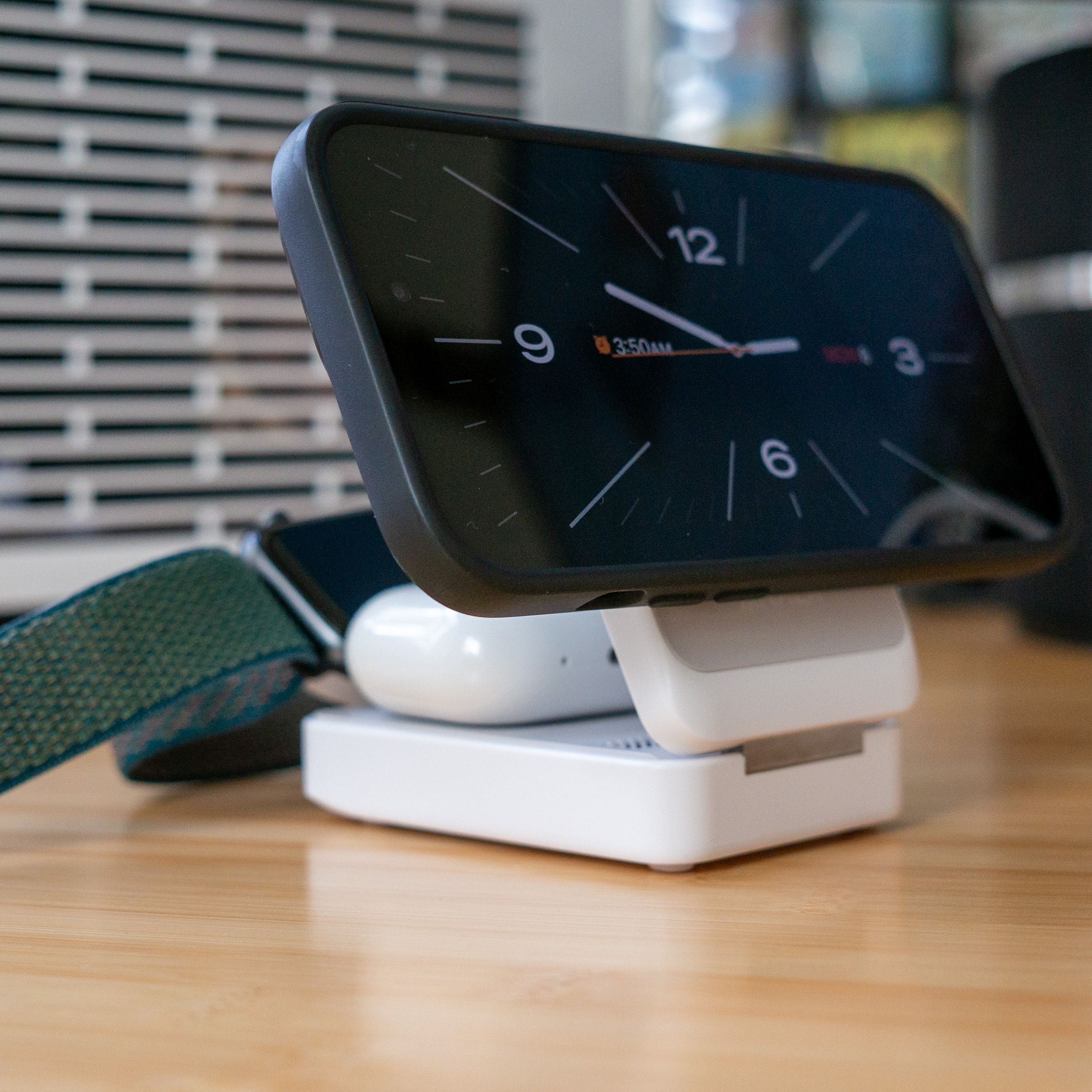 An iPhone 14, Apple Watch, and AirPods Pro all charging on a white portable Qi2 charger. The Apple Watch puck flips up from underneath.