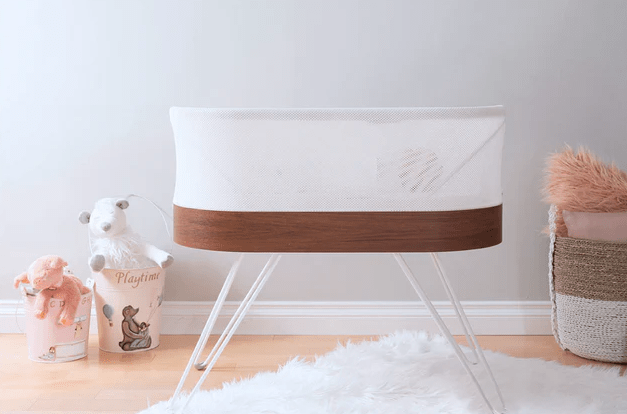 Picture of a Snoo bassinet on a white rug surrounded by baby toys.