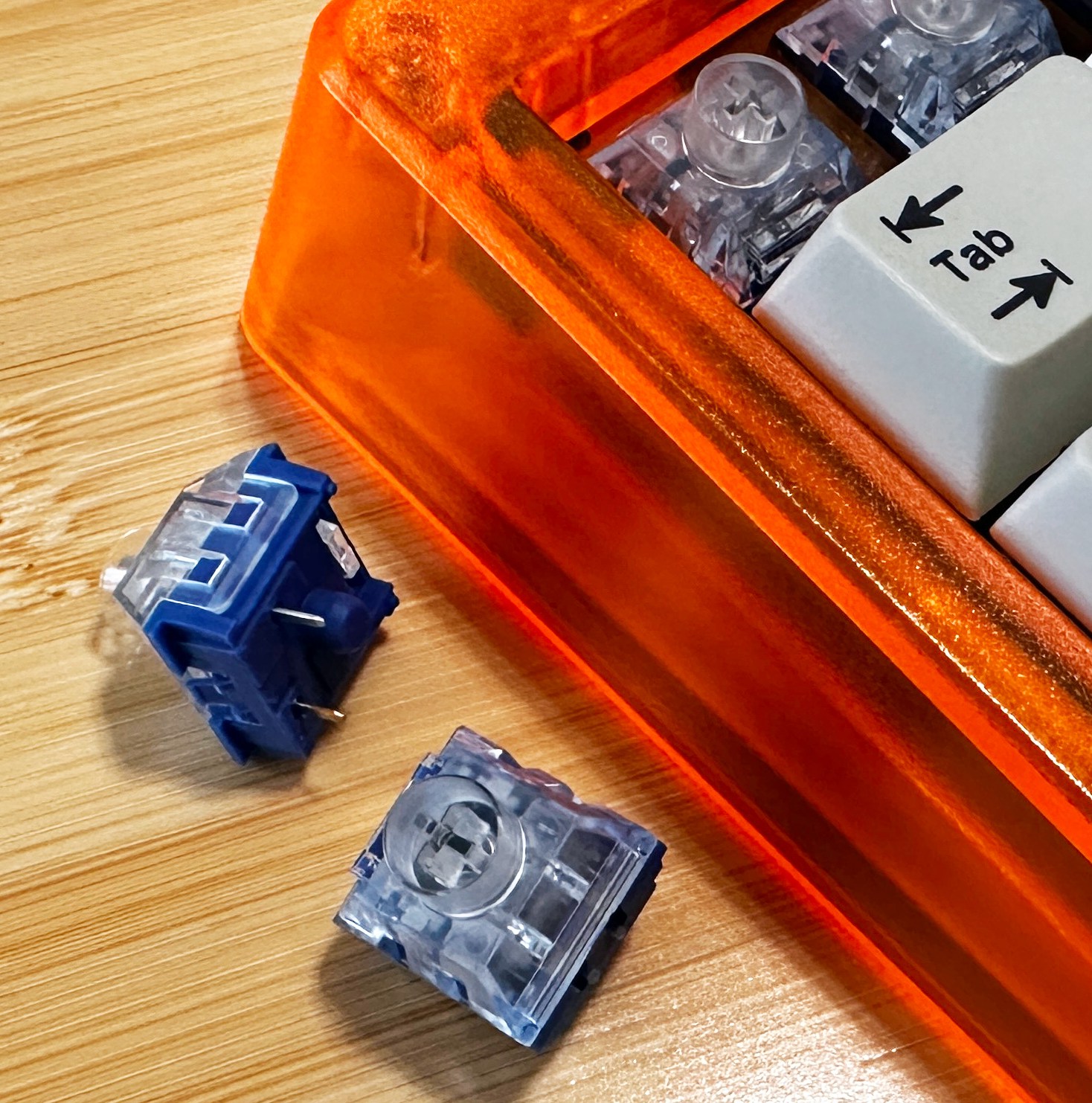 Close up of mechanical keyboard switches with clear tops and blue bases next to a bright orange keyboard. 