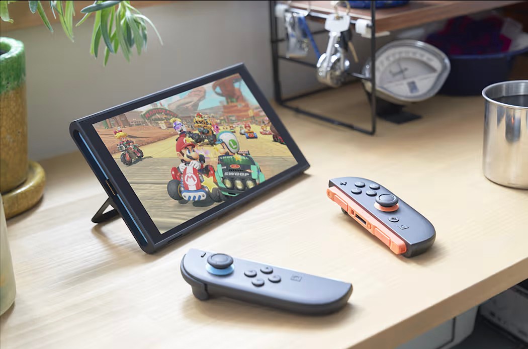 The Nintendo Switch 2 with a Mario game playing, display on, and Joy-Cons nearby on a desk.