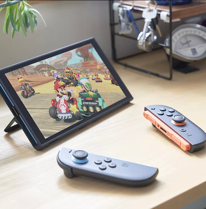 The Nintendo Switch 2 with a Mario game playing, display on, and Joy-Cons nearby on a desk.