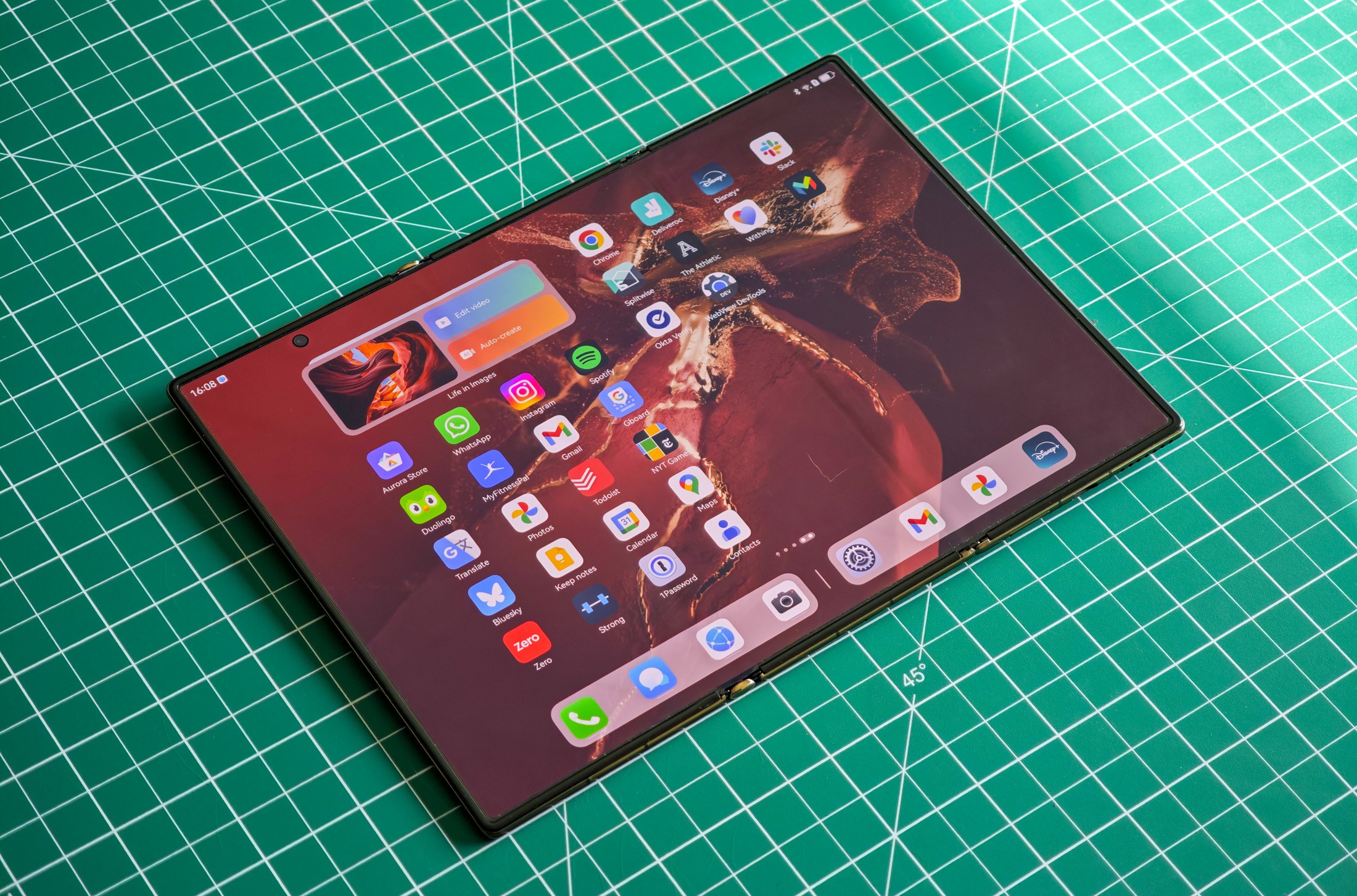 Huawei Mate XT flat on a green table fully unfolded.