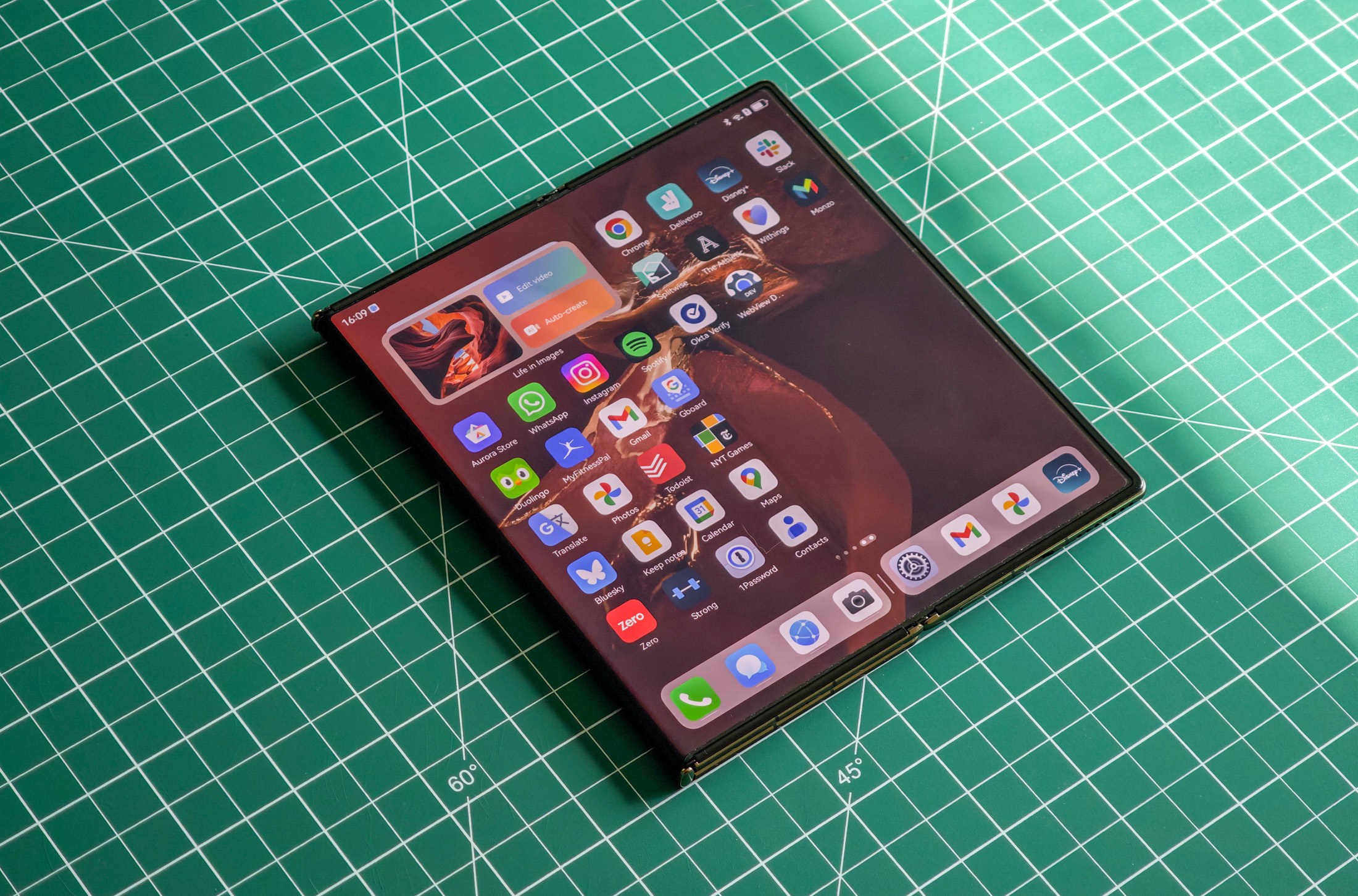 Huawei Mate XT flat on a green table partially unfolded.