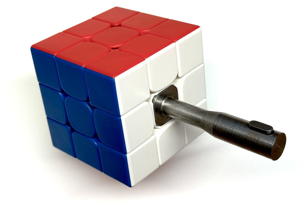A close-up of a Rubik’s Cube with a metal shaft attached to one side.