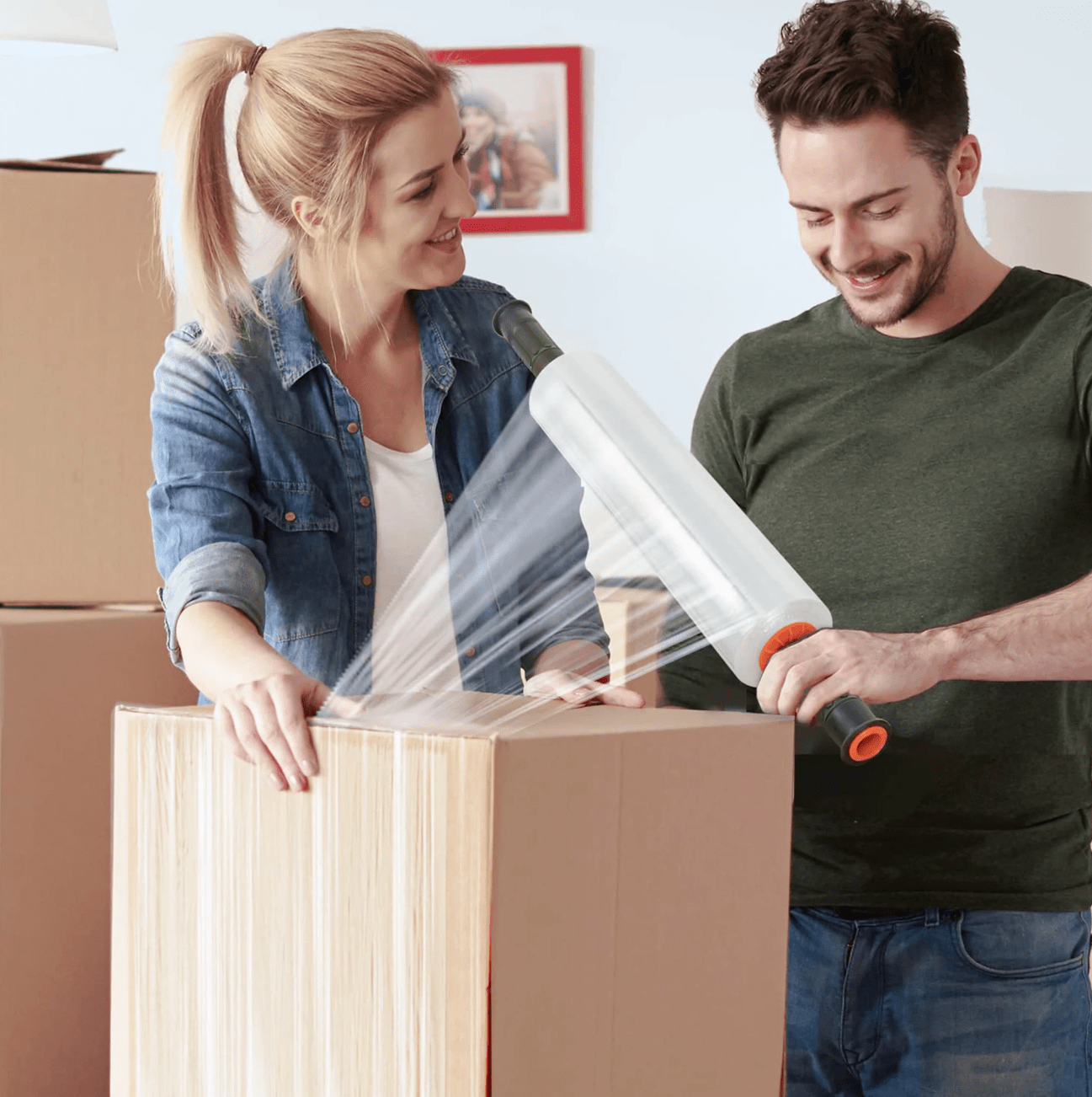 Man and woman with roll of shrink wrap covering a box.