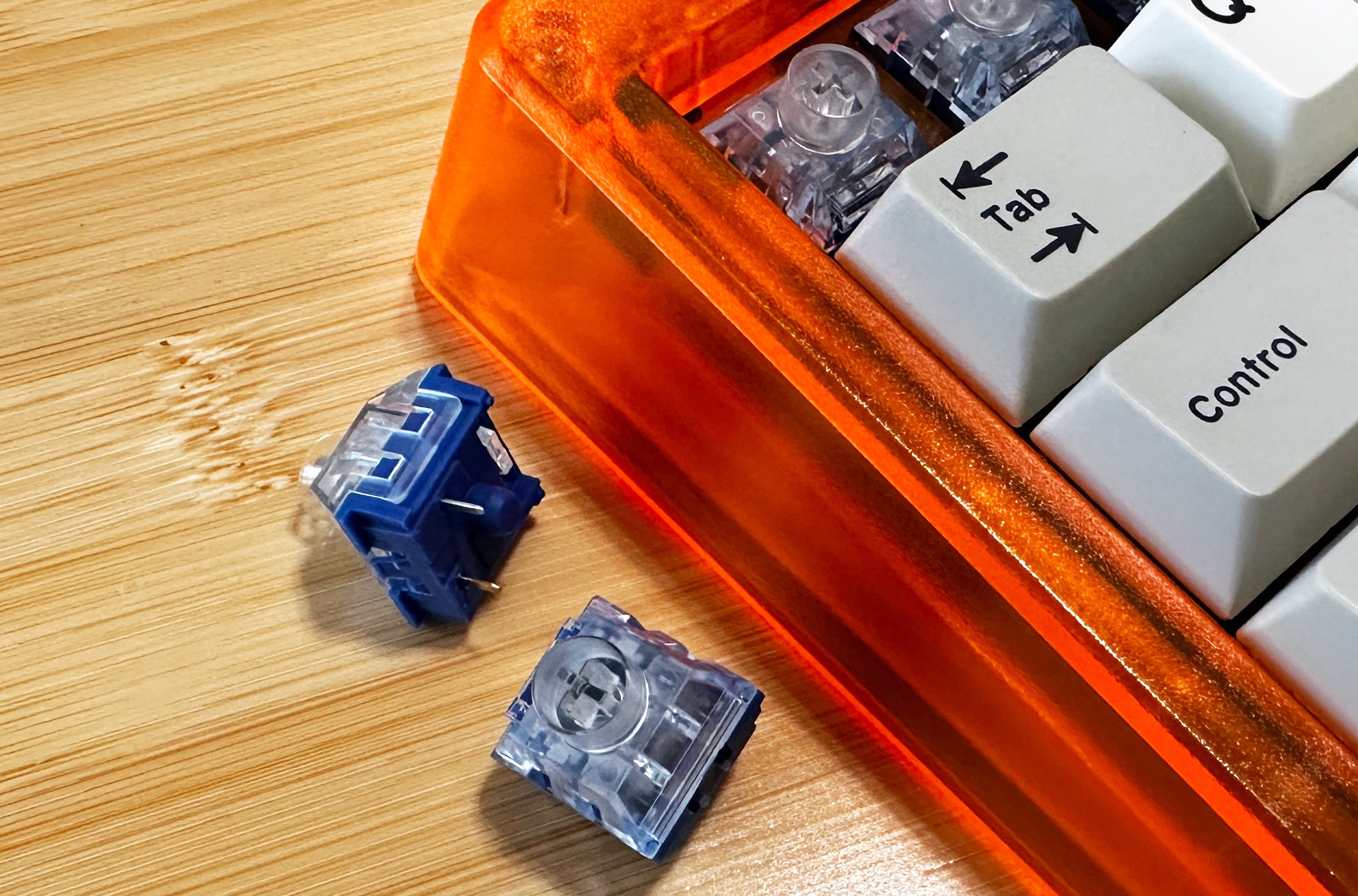Close up of mechanical keyboard switches with clear tops and blue bases next to a bright orange keyboard. 