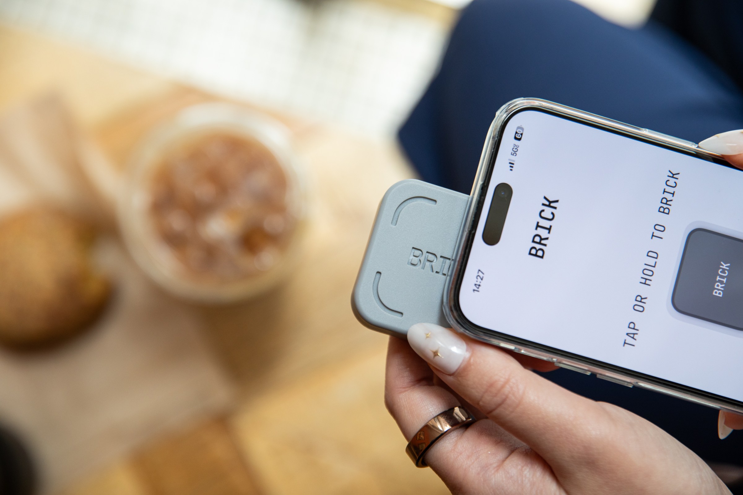Person tapping their phone to the Brick key. You can see a blurry coffee and pastry in the background.