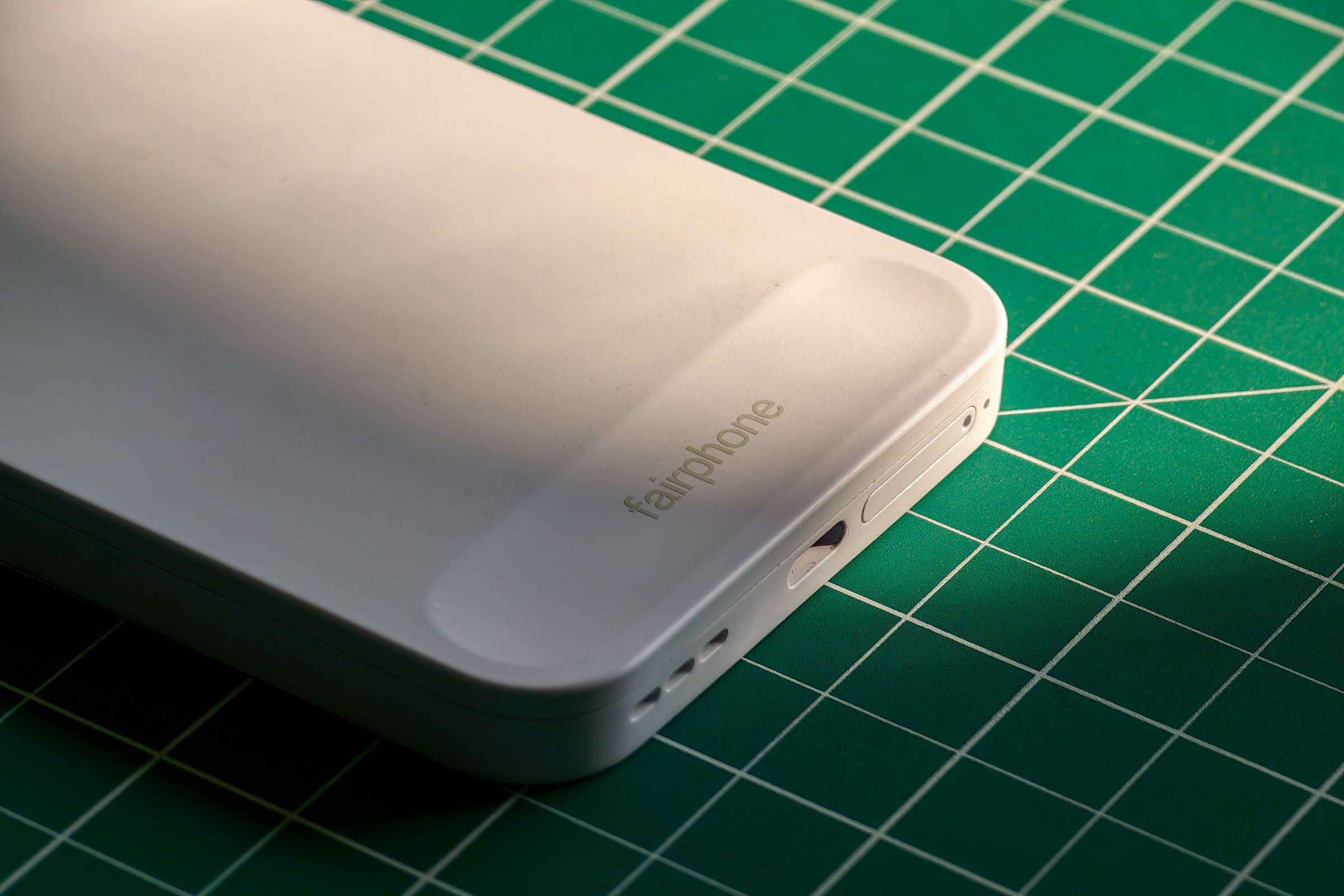 Photo of the Fairphone 6 lying on a green cutting mat with a closeup on the logo