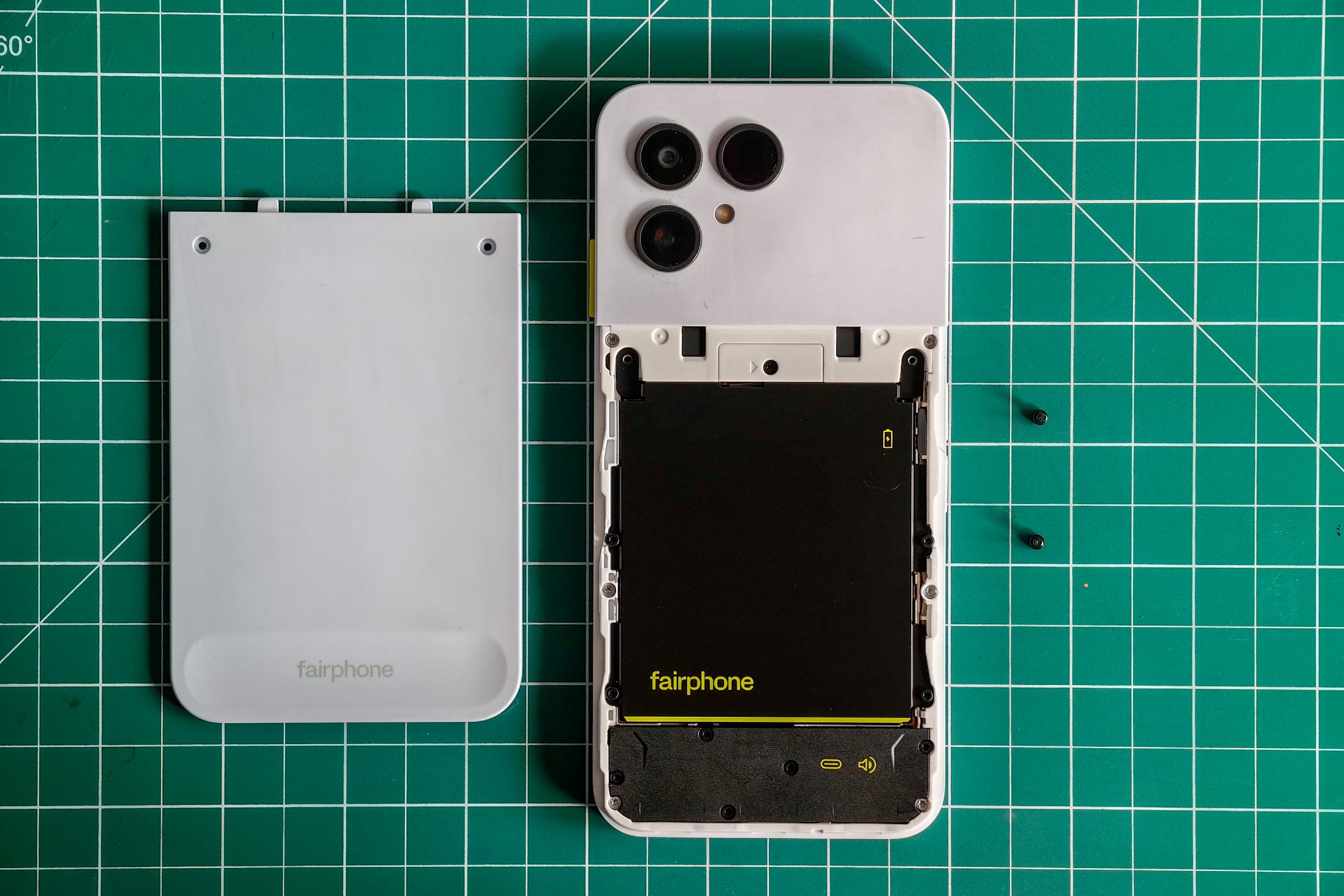 Photo of the Fairphone 6 lying on a green cutting mat with the back cover removed