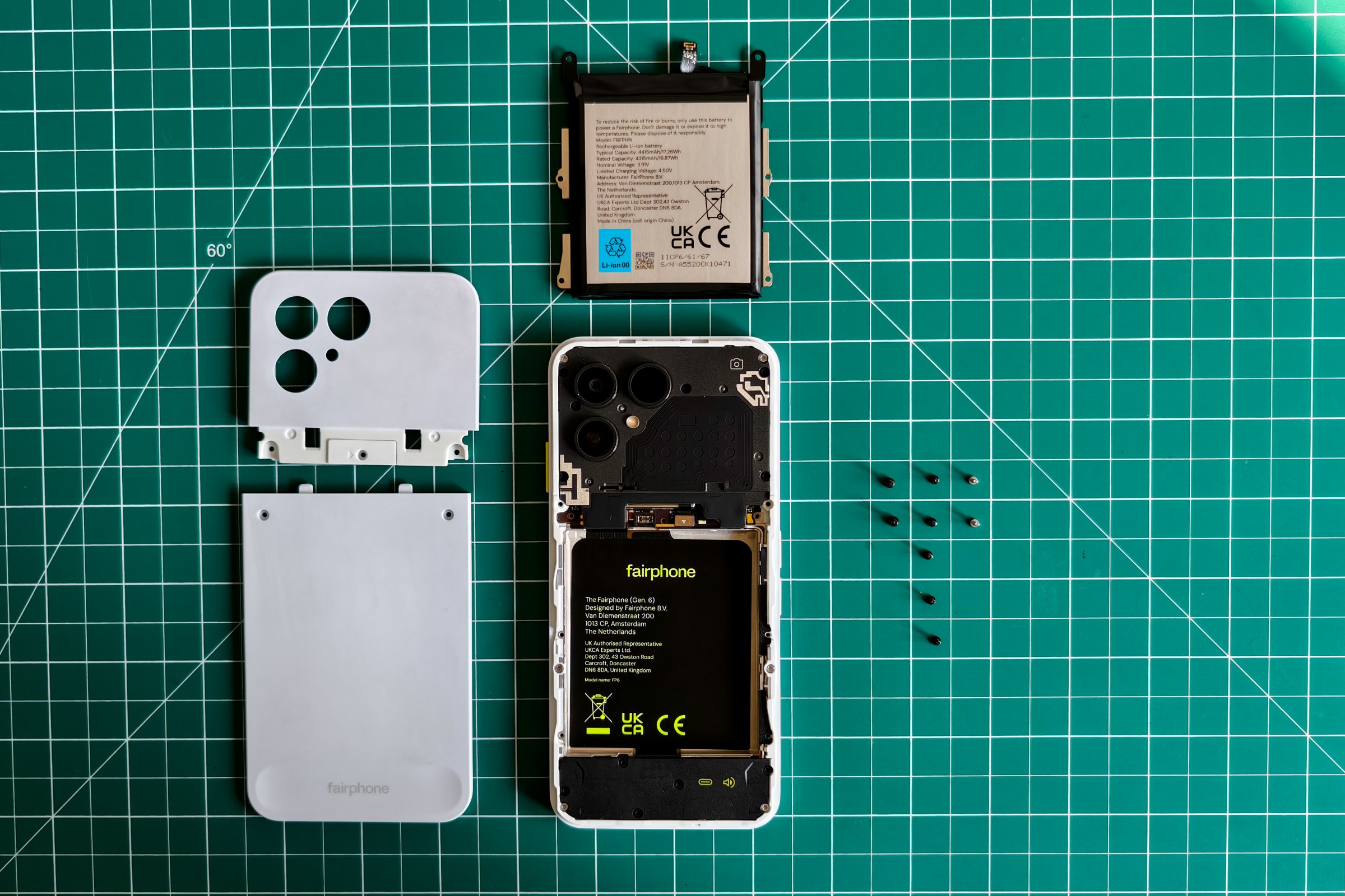 Photo of the Fairphone 6 lying on a green cutting mat with the back cover and battery removed