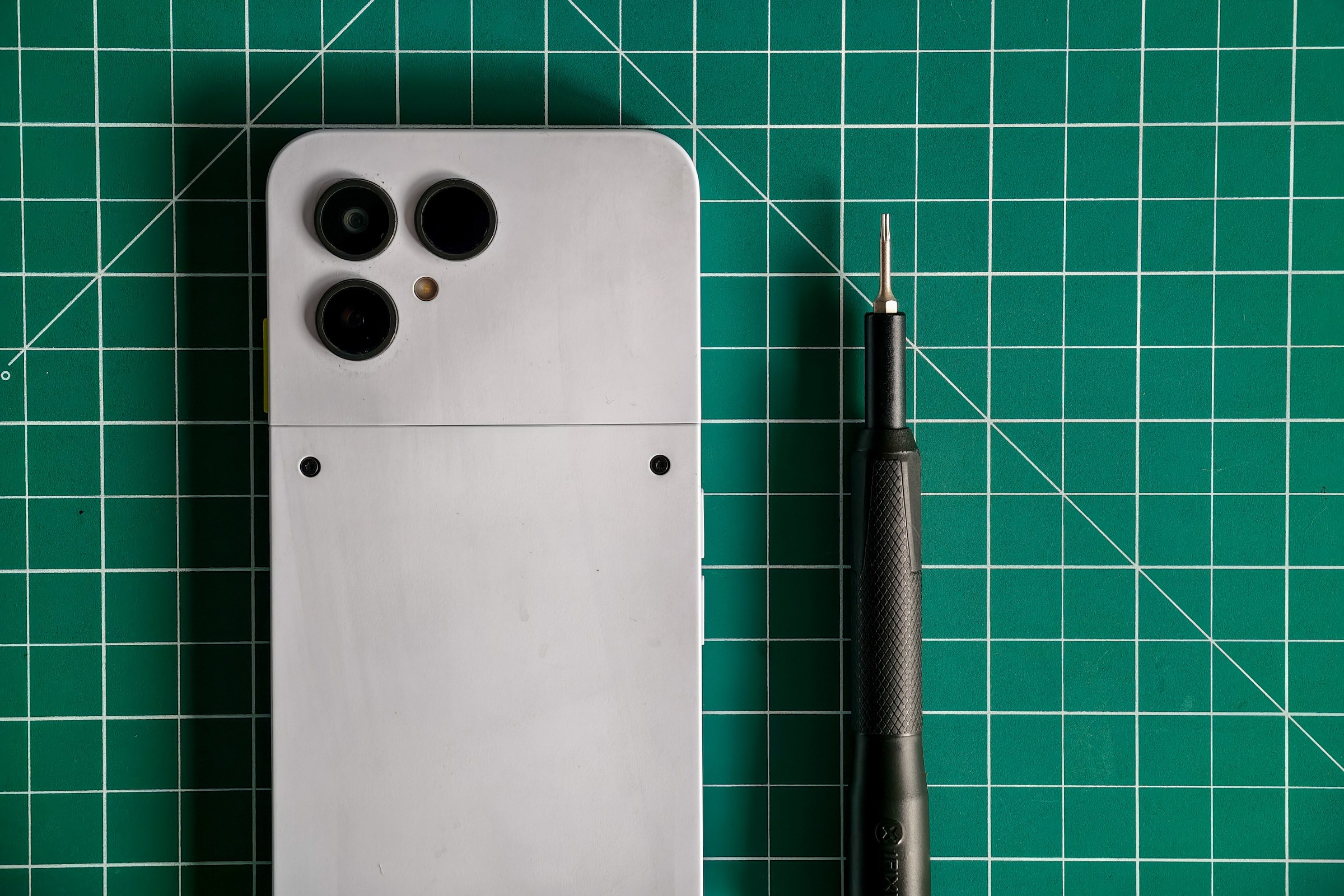 Photo of the Fairphone 6 lying on a green cutting mat with a Torx T5 screwdriver next to it