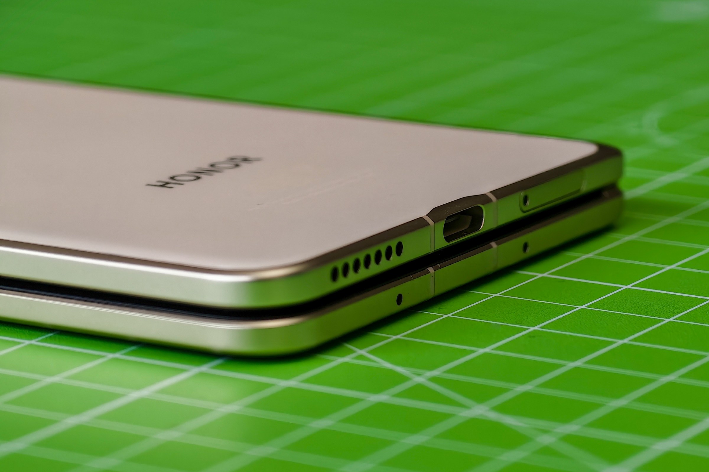 The Honor Magic V5 lying closed on a green cutting mat, showing the USB-C port