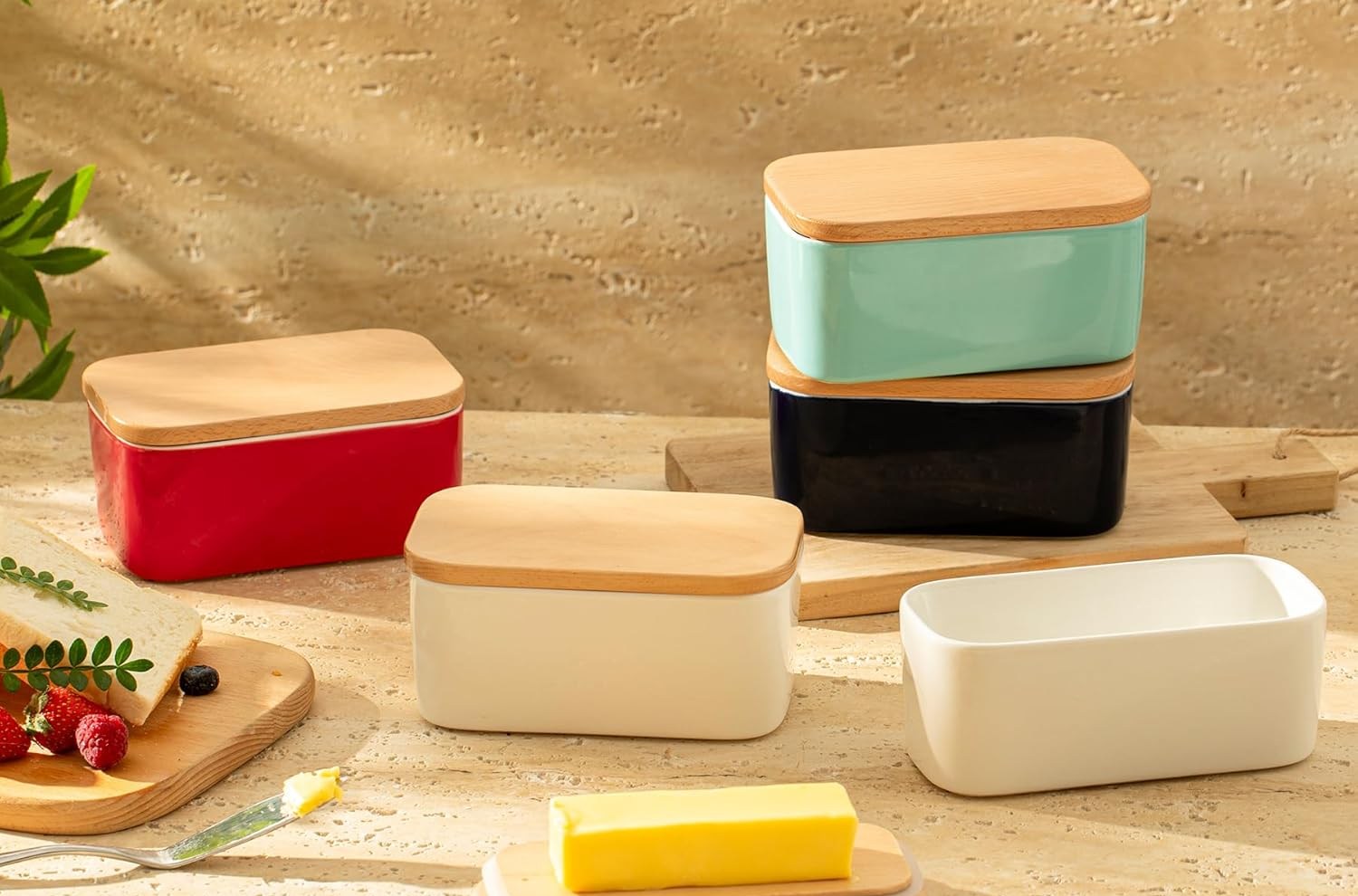 Several butter dishes with differently colored sides and a wooden top, with a stick of butter in front.