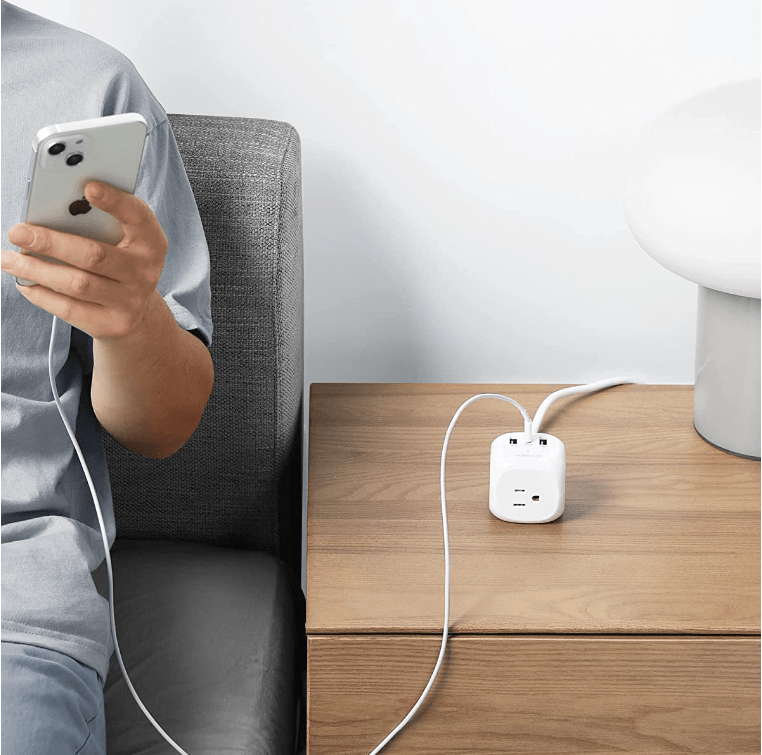 Anker cube power strip on table in between a person with a phone and a computer